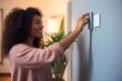 Woman adjusting smart thermostat control on wall.