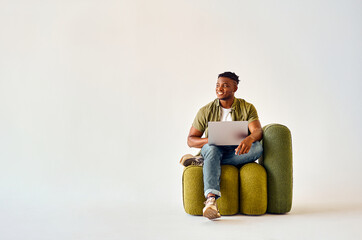 smiling african american man sitting on green design chair with portable laptop on knees over white 
