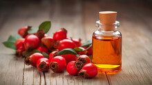 A radiant bottle of rosehip oil on rustic wooden surface, surrounded by fresh rosehips and leaves. Concept of natural skincare, herbal wellness solutions, beauty treatments and health practices