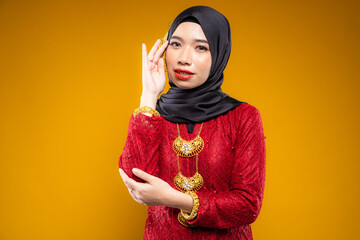 Wall Mural - Muslim woman wearing traditional wear red kebaya and hijab isolated on yellow background. Idul Fitri and hijab fashion concept.