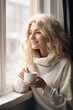Smiling young blond woman enjoying her coffee time by the window in a  cold day