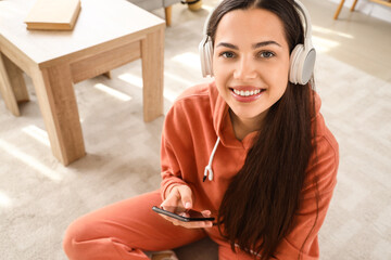 Wall Mural - Young woman in hoodie with headphones using mobile phone at home