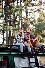 Happy couple relaxing on their van while camping in forest.