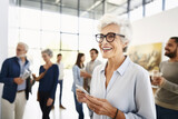 Fototapeta  - An elegant woman, a lady art critic and a professional gallery curator of an exhibition at a modern museum of contemporary art. In the background, a group of people discuss of artworks. Lifestyle