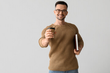 Wall Mural - Happy young man with cup of coffee and book on light background