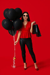 Canvas Print - Beautiful young Asian woman with shopping bags and balloons on red background. Black Friday sale