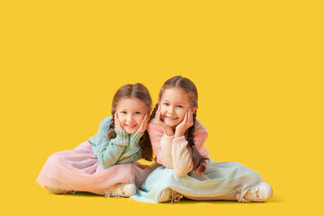 Wall Mural - Cute little girls in warm sweaters sitting on yellow background