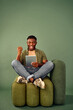 © HBS - Great deal. Handsome man sitting on soft green chair with crossed legs and gesturing from happiness while looking on tablet screen. Afro american guy celebrating great news and enjoying sincerely.