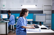 © DC Studio - Caucasian nurse sitting at clinic desk, writing data in appointment table list. Focused medical assistant employee wearing scrubs and stethoscope in clean, modern medical office