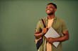 © HBS - Technology in education. Positive afro student carrying backpack and holding wireless laptop over green background with copy space. Handsome young guy in casual wear looking aside with beaming smile.