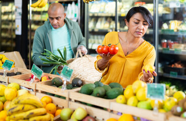 Interested Latin American woman making purchases in grocery store, looking for fresh vegetables and fruits..