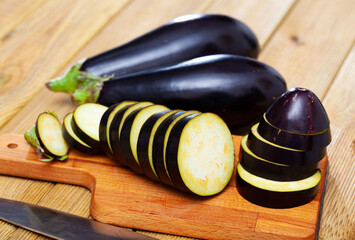 Wall Mural - Closeup of fresh eggplants with chopped slices on wooden surface. Healthy vegetarian ingredient