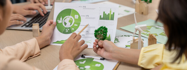 Wall Mural - Professional businessman interested in invested in green businesses when he see rising graph on table with environmental document and wooden block scatter around. Closeup. Focus on hand. Delineation.