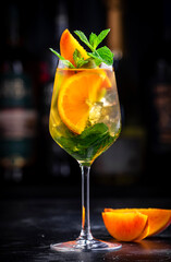 Wall Mural - White sangria alcoholic cocktail drink with viura spanish wine, peach, orange, lime and ice. Black bar counter background, steel bar tools and bottles