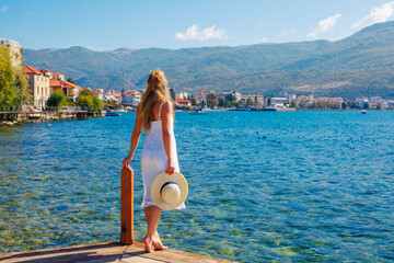 Wall Mural - Woman in white dress standing on wooden pier looking at the sea or lake (Macedonia, Ohrid lake, Albania)