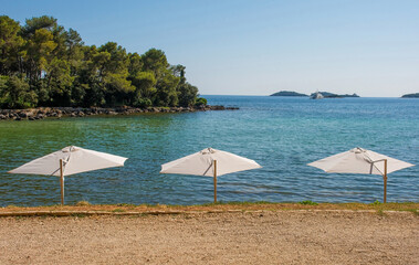 Wall Mural - White beach umbrellas on the coast at Cuvi Beach just south of Rovinj old town in Istria, Croatia