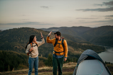 Wall Mural - Couple exploring a hill with backpacks, spotting a beautiful lake in the distance