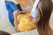 © Jelena Stanojkovic - Girl, phone and music on sofa to relax with headphones with smile, typing and happy on social media. Woman, smartphone and streaming song on internet while reading communication, blog post or email.