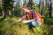 © DimaBerlin - Carefree man tourist hiker picking mushrooms berries in forest. Interested guy sitting near hill touching plants. Mushrooming, collecting edible products in woodland concept. Autumn harvesting crop.