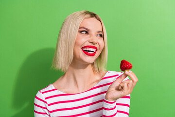 Sticker - Photo of cute young girl bob blonde hair toothy hollywood smile hold red strawberry interested look novelty isolated green color background