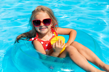 Wall Mural - Pretty little girl swimming in outdoor pool and have a fun with inflatable circle and drinking lemonade