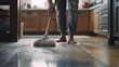 Close-up of a young man's hands gripping a mop as he skillfully cleans the floor of a contemporary kitchen