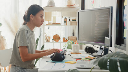Side view of professional young Asia girl IT development programmer typing on keyboard coding programming fixing data code on computer screen and laptop on table in workroom at house office.