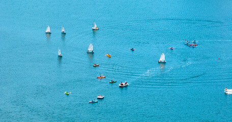 Variety of small colorful boats on gorgeous blue lake with sales and paddles aerial