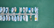 Aerial Downward View Of 22 Boats And Yachts On Single Pier On Teal Ocean Water