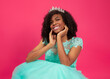 Cute hispanic girl celebrating her 16th birthday with a blue big dress in a pink background 