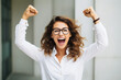 Portrait of overjoyed attractive woman standing with excited expression, raising fists, screaming, shouting yeah, celebrating her victory, success.