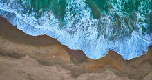 Downward Aerial Of Receding Green Ocean Waves On Top With Dark Tan Sandy Beach On Bottom