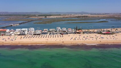 Wall Mural - Aerial view of the ocean coast and beach. Boats on the water and tourists relaxing on the beach as seen from a drone. Praia de Faro Algarve Portugal. Airport in the background.