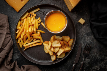 Wall Mural - Fried potatoes, fries with cheese sauce on a black plate, dark table..Beer snacks, potato snacks in assortment Beer snacks, potato snacks in assortment