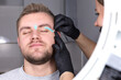 © Iuliia - Depilation of the face with warm wax. A female eyebrow stylist applies melted wax to the eyebrows of a young unshaven blond man. Cosmetology for men