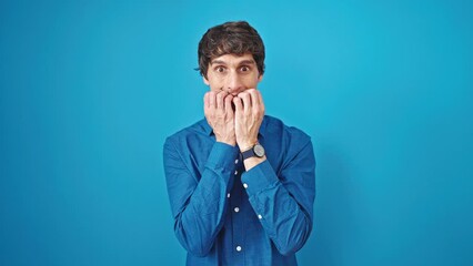 Poster - Young hispanic man standing with nervous expression looking watch over isolated blue background