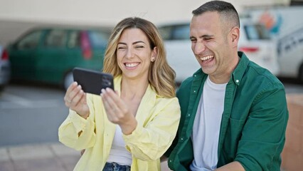 Poster - Man and woman couple sitting on bench watching video on smartphone at street