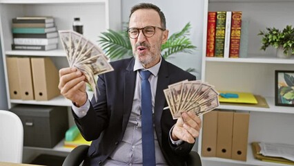 Wall Mural - Hispanic, middle-age, grey-haired, suit-clad business worker ecstatically kissing banknotes in his office, instinctively smiling while basking in the joys of professional success.