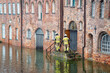 High water flooding the old town of Lubeck when the river Trave overflows its banks, specialists control water level and danger at a historic building of red brick architecture