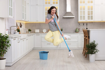 Sticker - Enjoying cleaning. Happy woman in headphones jumping with mop in kitchen