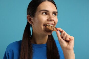 Young woman with chocolate chip cookie on light blue background, closeup