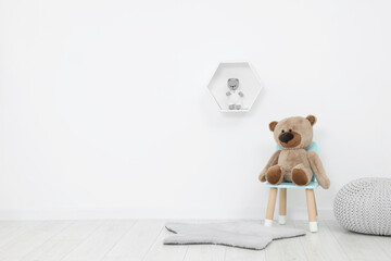 Wall Mural - Teddy bear sitting on chair near white wall in playroom, space for text. Stylish kindergarten interior