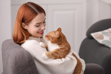 Wall Mural - Happy woman with her cute cat in armchair at home