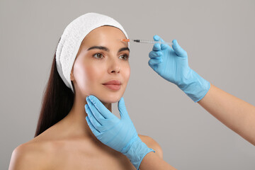 Wall Mural - Doctor giving facial injection to young woman on light grey background. Cosmetic surgery