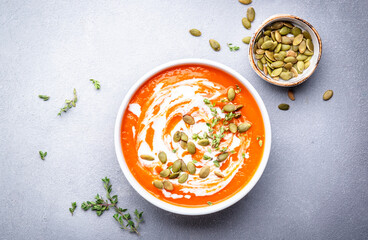 Wall Mural - Autumn slow comfort food. Pumpkin soup puree with seeds, coconut cream and thyme.. Healthy vegetarian food. White soup bowl on gray table background. Top view