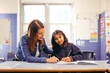 © Austockphoto - Aboriginal female school teacher sitting with her student in the classroom