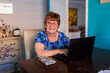 © Austockphoto - Smiling senior woman using laptop in dining room of house