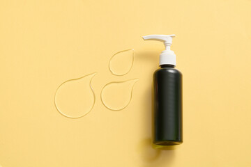 Wall Mural - An unlabeled black lotion pump bottle, a few drops of translucent dense texture on a yellow background. Skin care product, smoothing serum. Empty space for text and image design.