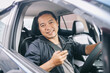 Portrait of friendly Asian online taxi driver looking at camera smiling and holding smart phone while sitting in car