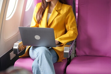 Asian woman sitting on airplane playing with cell phone and looking out window on vacation travel concept Talk about business on airplanes, listen to music, watch movies, relax, travel.